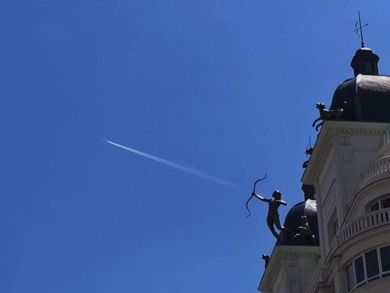 Statue Cupidon avec un avion dans le ciel en guise de flèche.