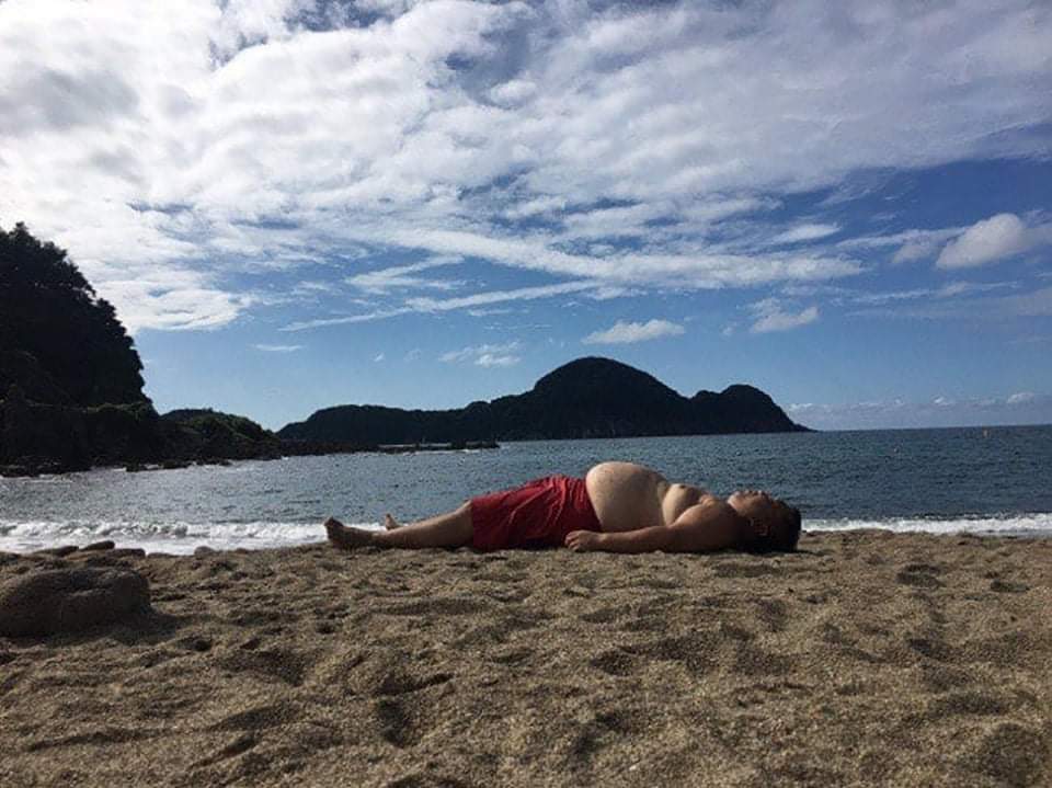 Un homme allongé sur la plage de la même forme qu'une montagne en arrière plan.